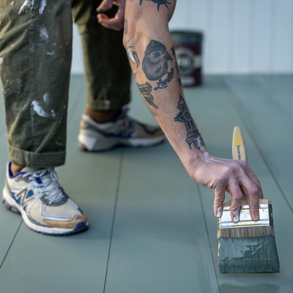 Ein Maler streicht den Holzboden mit einem Pinsel von Farrow & Ball Farbe