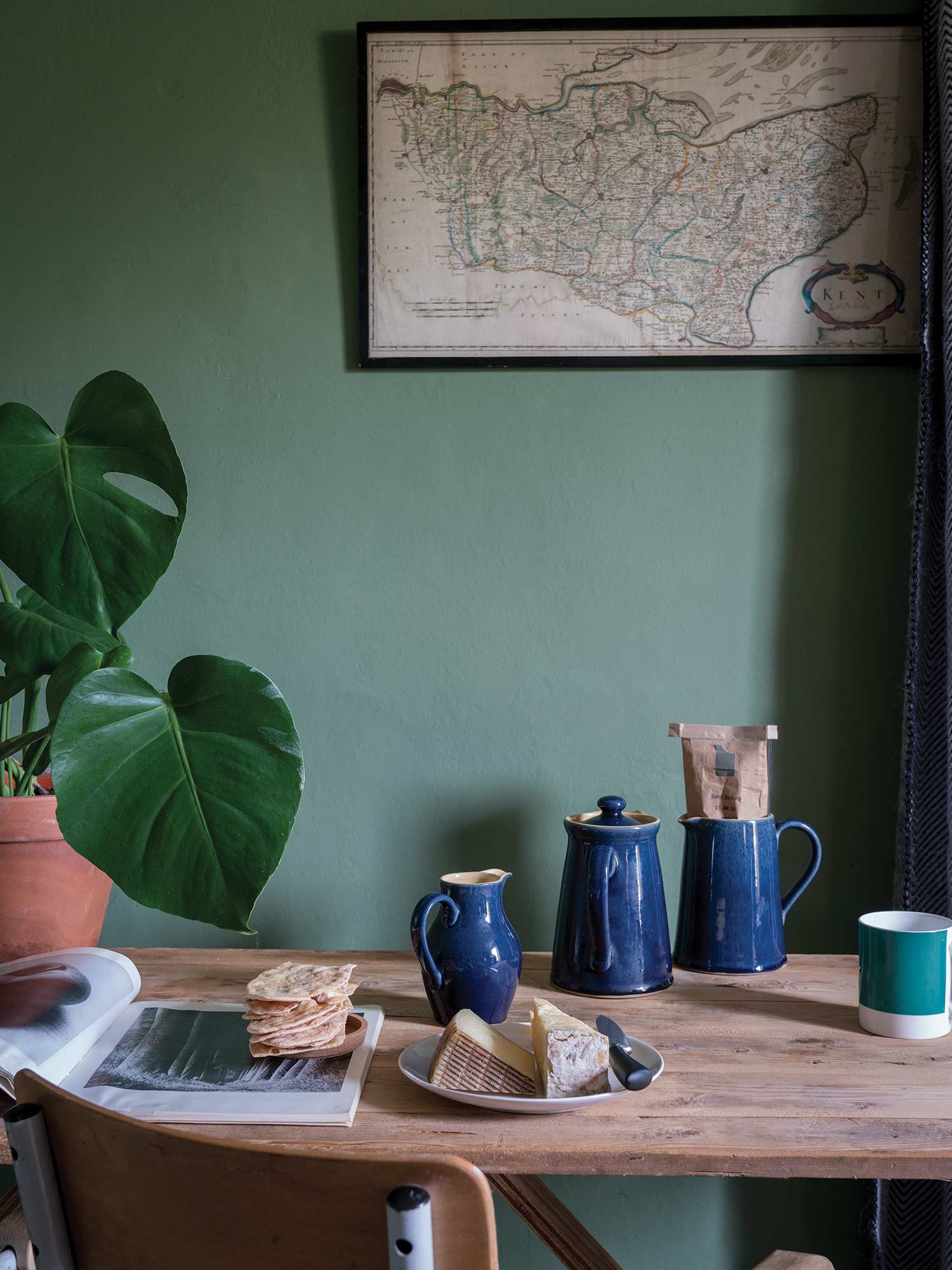 Esszimmer mit Calke Green No. 34 von Farrow & Ball. Sattes Salbeigrün an den Wänden mit Holztisch und blauem Keramikgeschirr.