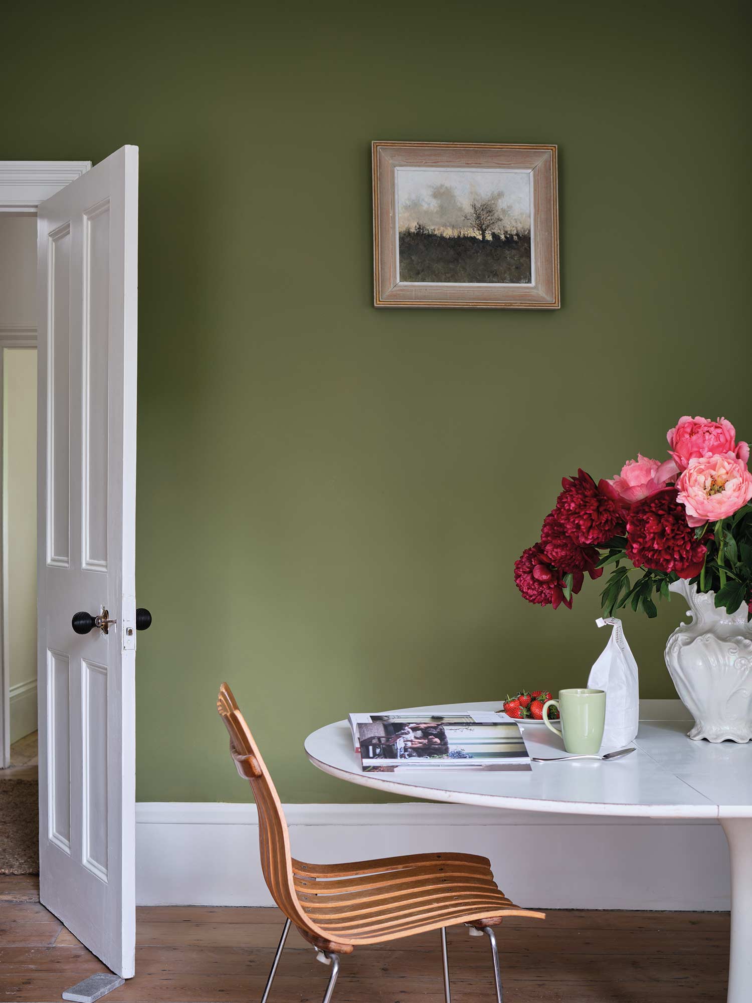 Esszimmer mit Sap Green No. 199 von Farrow & Ball. Helles Olivgrün an den Wänden mit weißem Tisch und üppigem Blumenstrauß.