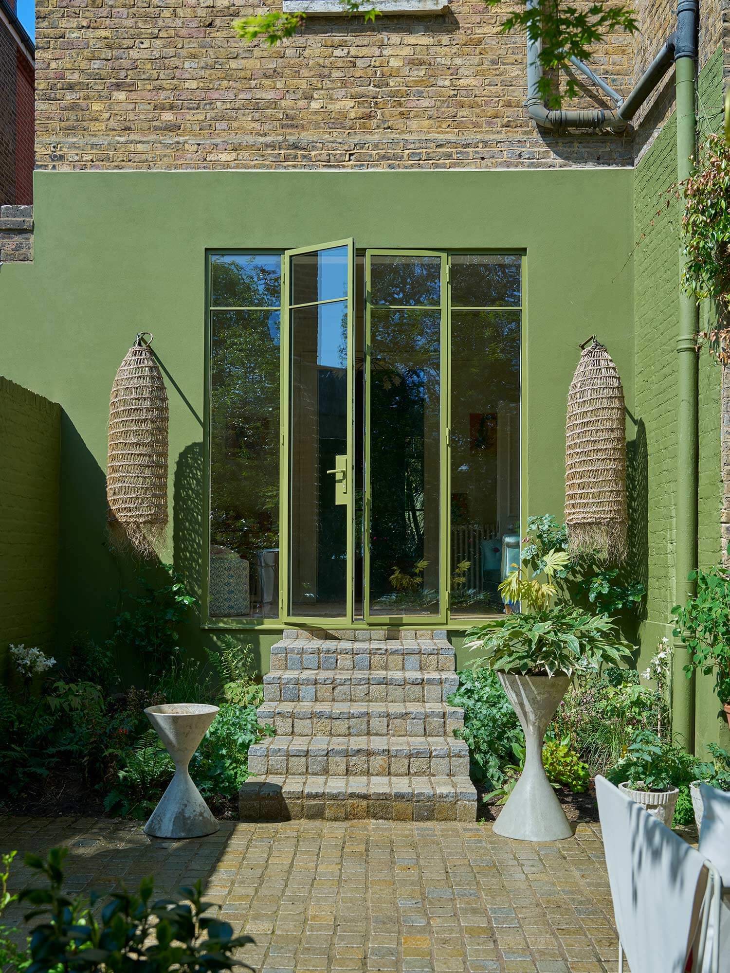Hausfassade mit Bancha No. 298 von Farrow & Ball. Olivgrüner Mid-Century Ton auf Mauerwerk mit Fensterrahmen und Regenrohr in demselben Ton.